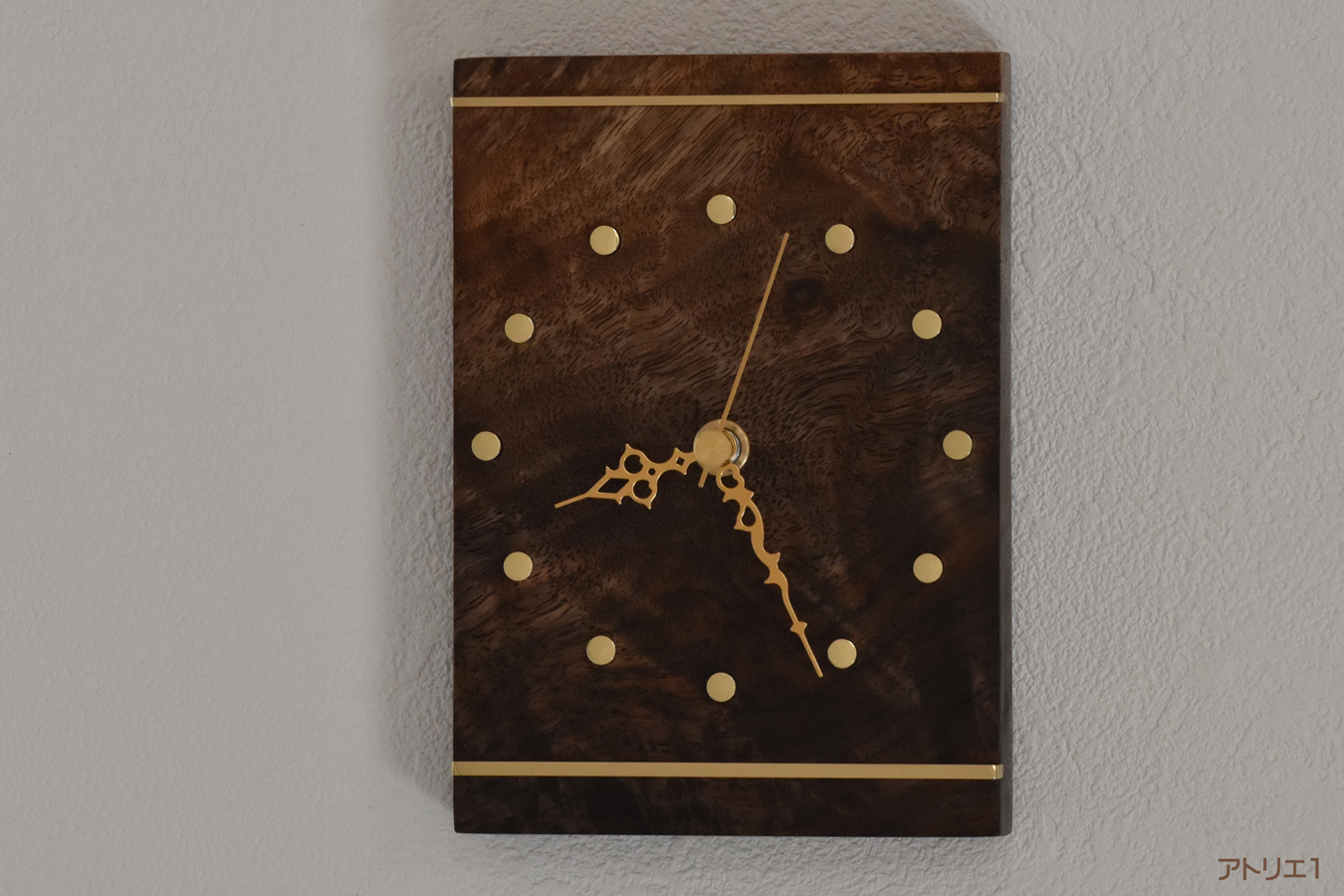 波状・カーリーの木目に立ち昇るような杢があるブラックウォルナットを長方形に切り出し、磨き上げた真鍮を上下に配したカードのキングをイメージして作ったコンパクトながら重厚感のある掛け時計です。