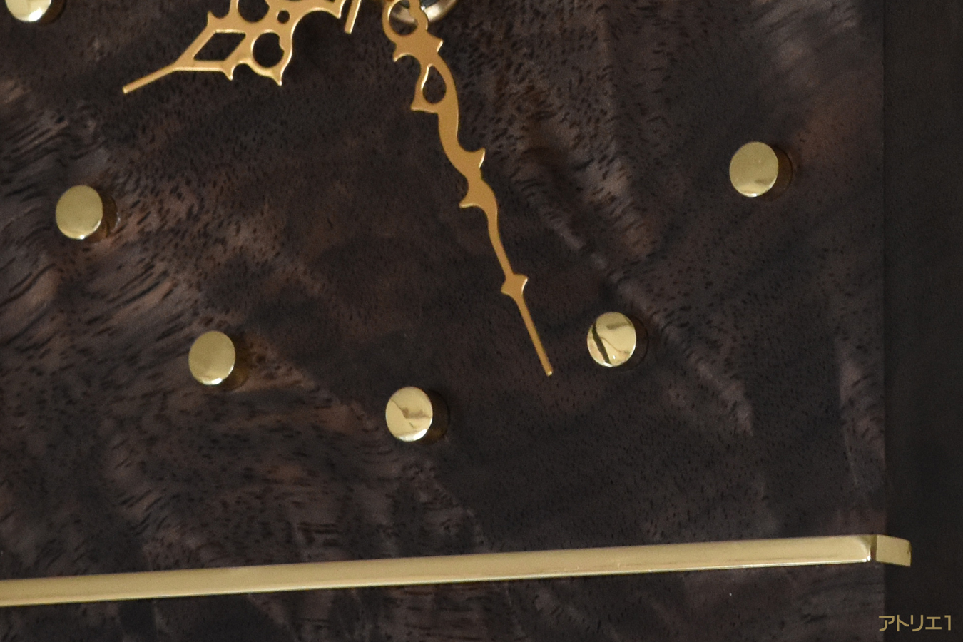 チーク・マホガニーと共に世界の三大銘木と言われているブラックウォルナットを用い、その流れるような木目とそれに交わるシルクのように輝く杢を磨き上げた真鍮のラインで抑え、磨き上げた時刻目盛りの真鍮と共にゴージャス感のあるデザインに仕上げました。