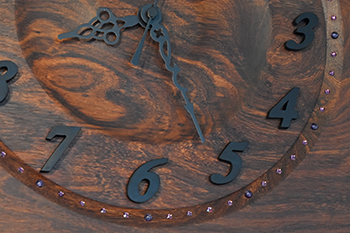 時刻の数字は斜体の字体を採用しおしゃれな印象にしてあります。時刻の数字には正倉院の宝物にも黒檀が見られるほど古来より珍重されている黒檀を切り出して時刻を見やすくしています。斜めに彫り込んだ斜面に分目盛りとしてアメジスト色のスワロフスキーを配しており、5分おきに4ｍｍのアメジストの天然石にしました。