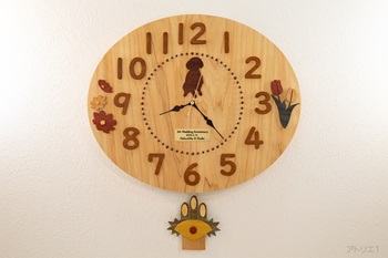 天然檜を長径42㎝短径35㎝の楕円に切り出した振り子時計です。振り子は、1ヶ月毎に交換できるように12か月分作成しました。前面にはご希望のトイプードルとお嬢様二人を表す花と木婚式の記念のプレートを設置しました。