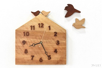 杢のある美しいカバザクラの木をおうちの形に切り出した掛け時計です。おうちの屋根に小鳥が乗っている幸せな形にした可愛い時計に仕上げました。追加でご依頼いただきました時計本体の小鳥を羽ばかせたデザインのウォールデコも時計本体の小鳥と同じ木で制作しました。