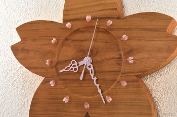 時刻目盛りの内側を丸く一段彫り込んで木目の変化を楽しむデザインにしました。時刻目盛りは桜の花びらの形のガラスピンにし、針はアラベスクデザインでピンクにしました。