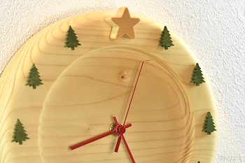 木肌が白いスプルースを丸く切り出し、周囲をラウンドさせた柔らかいフォルムのベースの時計に「１２時」に星を、「１時」～「１１時」にモミの木を配置しました。