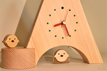 三角形に切り出した天然檜の底辺をアーチ型に切り抜き、ブランコに乗るヒヨコをあしらった置き時計です。ヒヨコは木目の詰まった木曽檜で作ってあり、くちばしはブラックウオルナットです。時計の時刻目盛りはグリーンのスワロフスキーで、12時のみ大きめのものを使用、赤い針とベースの白っぽい天然檜でポップなイタリアンカラーに仕上げましたので、インテリアの一品として飾っても楽しいデザインです。ブランコに乗るヒヨコは軽く指で押すと、本物のブランコのように前後に揺れます。