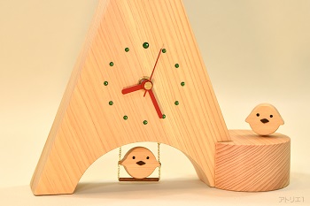 三角形に切り出した天然檜の底辺をアーチ型に切り抜き、ブランコに乗るヒヨコをあしらった置き時計です。ヒヨコは木目の詰まった木曽檜で作ってあり、くちばしはブラックウオルナットです。時計の時刻目盛りはグリーンのスワロフスキーで、12時のみ大きめのものを使用、赤い針とベースの白っぽい天然檜でポップなイタリアンカラーに仕上げましたので、インテリアの一品として飾っても楽しいデザインです。ブランコに乗るヒヨコは軽く指で押すと、本物のブランコのように前後に揺れます。