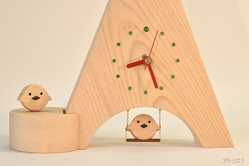 三角形に切り出した木曽檜の底辺をアーチ型に切り抜き、ブランコに乗るヒヨコをあしらった置き時計です。ヒヨコは木目の詰まった木曽檜で作ってあり、くちばしはブラックウオルナットです。時計の時刻目盛りはグリーンのスワロフスキーで、12時のみ大きめのものを使用、赤い針とベースの白っぽい天然檜でポップなイタリアンカラーに仕上げましたので、インテリアの一品として飾っても楽しいデザインです。ブランコに乗るヒヨコは軽く指で押すと、本物のブランコのように前後に揺れます。
