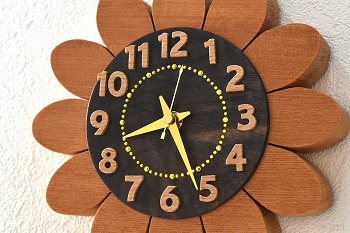 インテリ掛け時計としての質感のバランスを考慮して、中心部はブラックウオルナットの木を使用しています。そして、ひまわりの管状花をスワロフスキーを使用して表現しています。時刻の数字は、ブナの木をひとつずつ糸鋸で切り出しました。