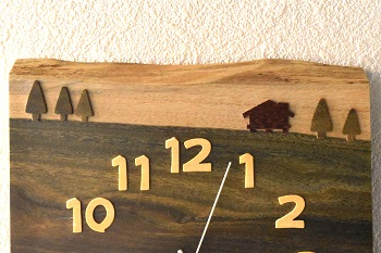 時刻目盛りは草原のイメージにマッチするようにデザイン性の高いポップな字体の数字を「黄楊」から切り出しました。また、草原の彼方には山小屋を「チンチャン」から切り出し、また、ベースと同じパロサントを木立の形に切り出して配しました。針は、はっきりと見やすいようにわずかにラウンドした細い棒状の白い針を採用しています。