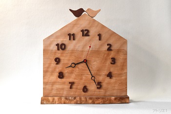 杢のある美しいカバザクラの木をおうちの形に切り出した掛け時計です。おうちの屋根に小鳥が乗っている幸せな形にデザインした可愛い時計に仕上げました。棚でご使用になれるように置き台を準備いたしました。