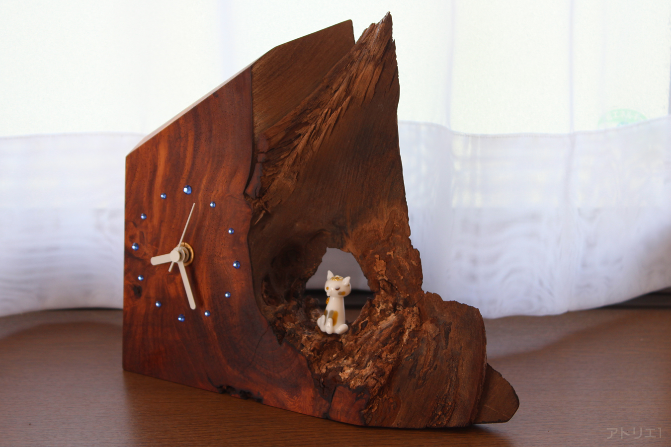 カリンの美しい木目と木の洞（うろ）がガラス細工の猫とスロフスキーサファイアの輝きで幻想的な世界を感じさせる木の置き時計です。