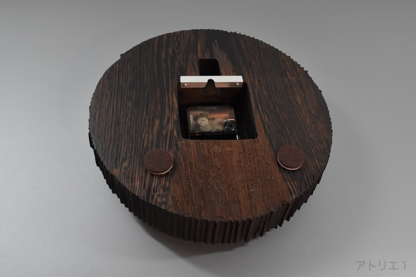 ムーブメントは、静かな時の流れを感じられるようクオーツ時計のスイープを使用しています。壁へのあたり部分は、壁を保護するようにフェルト仕上げになっています。また、壁に取り付ける際に使用するフックなども背面板に当たらないように取り付け金具周辺も彫り込んであります。ムーブメントのまわりに隙間があるのは、将来のムーブメント交換の際にどのようなものとでも交換できるようにとの配慮から大きめに加工しています。