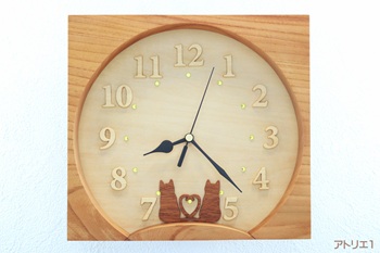 お互いの尻尾でハートの形を作って仲良く並んだ２匹の猫はマホガニーを薄い板状にしたものから糸鋸で切り出しました。時刻数字には、アフリカのアユースという淡いクリーム色の木から、ひとつひとつ切りだしたので、月の風情を妨げることなく、陰影で数字がわかるようにしました。